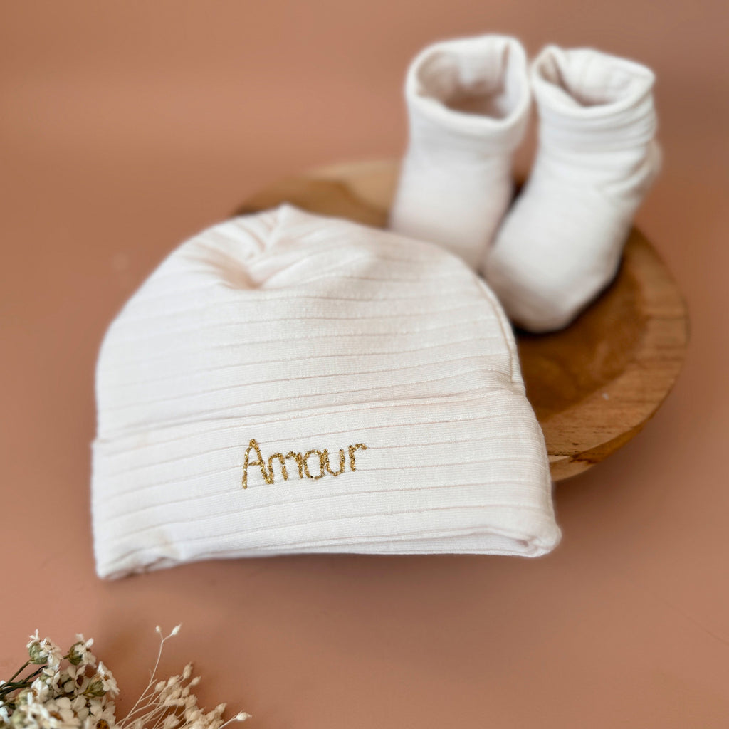 Le bonnet de naissance personnalisé pour bébé en maille côtelée est l'accessoire idéal pour les premiers jours de votre nouveau-né. Confectionné avec soin dans un jersey de coton côtelé , ce bonnet offre à votre bébé douceur et confort incomparables. Il est fabriqué dans l’un de nos ateliers partenaires français. Nous conseillons ce modèle de bonnet plus léger pour les naissances prévues de mai à septembre.  Un cadeau parfaitement adapté pour accueillir votre petit trésor dans le monde avec tendresse et dou