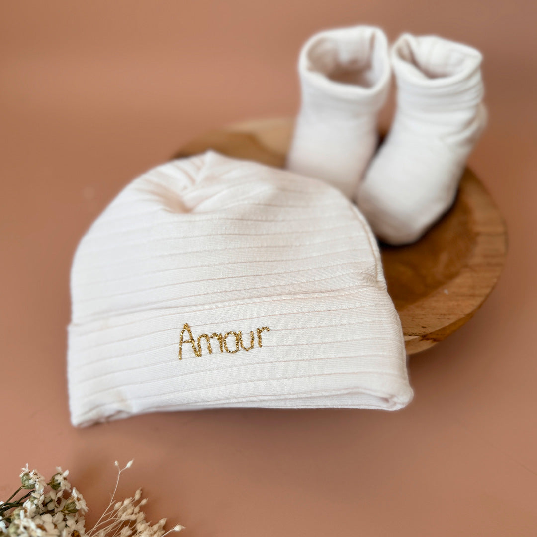 Le bonnet de naissance personnalisé pour bébé en maille côtelée est l'accessoire idéal pour les premiers jours de votre nouveau-né. Confectionné avec soin dans un jersey de coton côtelé , ce bonnet offre à votre bébé douceur et confort incomparables. Il est fabriqué dans l’un de nos ateliers partenaires français. Nous conseillons ce modèle de bonnet plus léger pour les naissances prévues de mai à septembre.  Un cadeau parfaitement adapté pour accueillir votre petit trésor dans le monde avec tendresse et dou