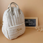 Voici notre tout nouveau sac à dos maternelle, pensé et confectionné en France pour accompagner vos tout-petits dans leurs premières journées d'école. Ce modèle délicat est réalisé en gaze de coton matelassée écrue, ornée de petites feuilles dorées qui lui donnent une allure douce et poétique. La grande particularité de ce sac ? Il est personnalisé avec le prénom de votre enfant, brodé à la main en fil doré sur la poche avant. Un détail unique, raffiné, et tellement précieux pour marquer les affaires de vot