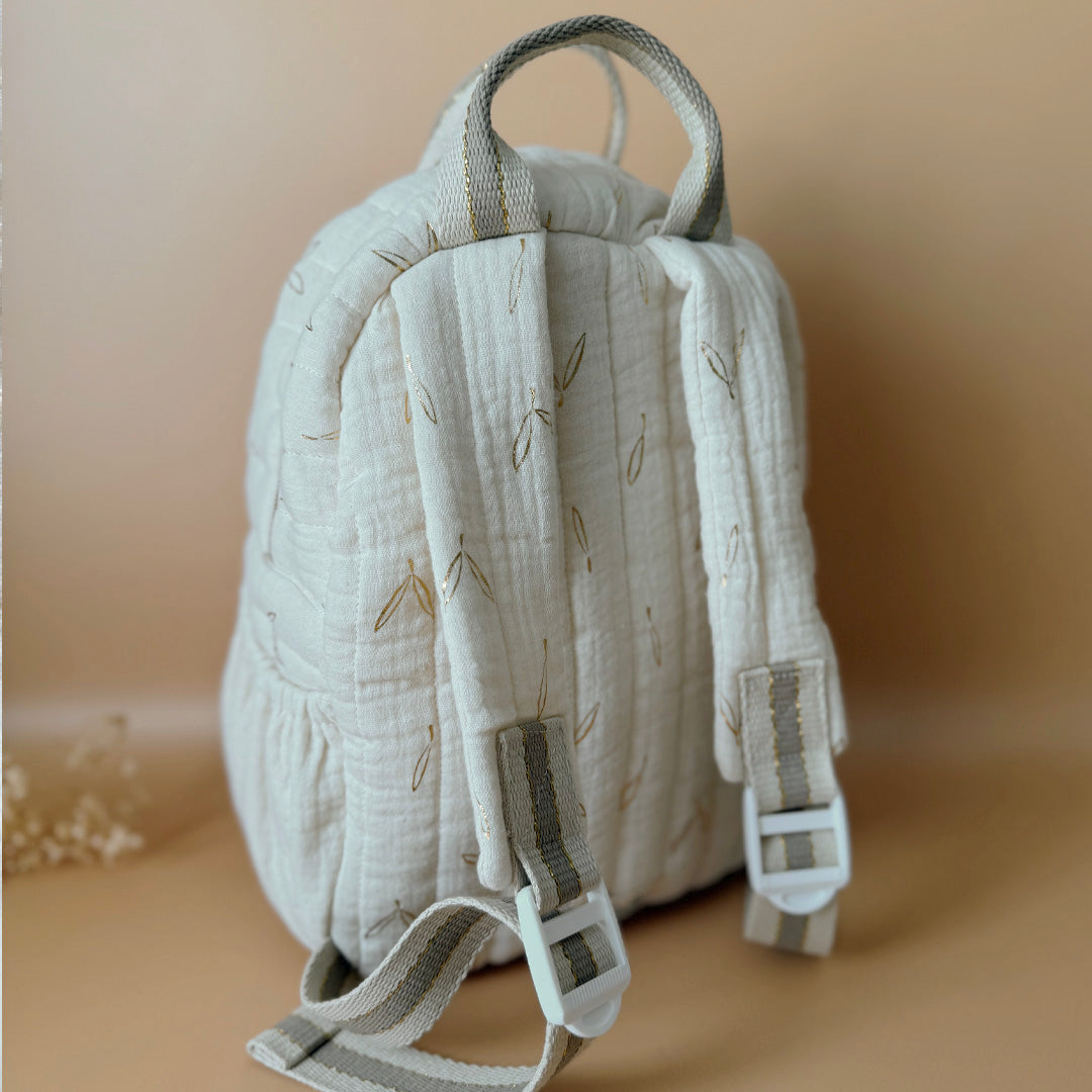 Voici notre tout nouveau sac à dos maternelle, pensé et confectionné en France pour accompagner vos tout-petits dans leurs premières journées d'école. Ce modèle délicat est réalisé en gaze de coton matelassée écrue, ornée de petites feuilles dorées qui lui donnent une allure douce et poétique. La grande particularité de ce sac ? Il est personnalisé avec le prénom de votre enfant, brodé à la main en fil doré sur la poche avant. Un détail unique, raffiné, et tellement précieux pour marquer les affaires de vot