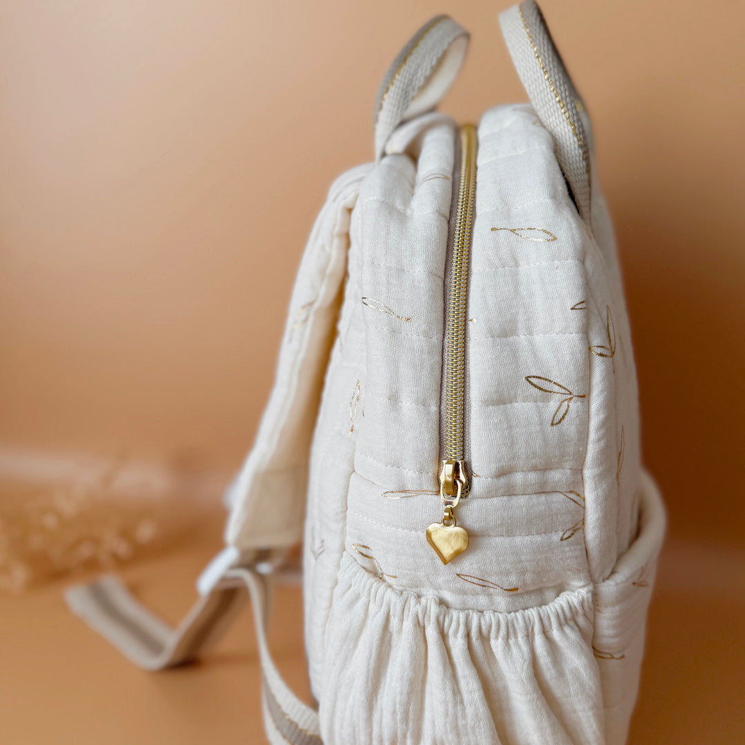 Voici notre tout nouveau sac à dos maternelle, pensé et confectionné en France pour accompagner vos tout-petits dans leurs premières journées d'école. Ce modèle délicat est réalisé en gaze de coton matelassée écrue, ornée de petites feuilles dorées qui lui donnent une allure douce et poétique. La grande particularité de ce sac ? Il est personnalisé avec le prénom de votre enfant, brodé à la main en fil doré sur la poche avant. Un détail unique, raffiné, et tellement précieux pour marquer les affaires de vot