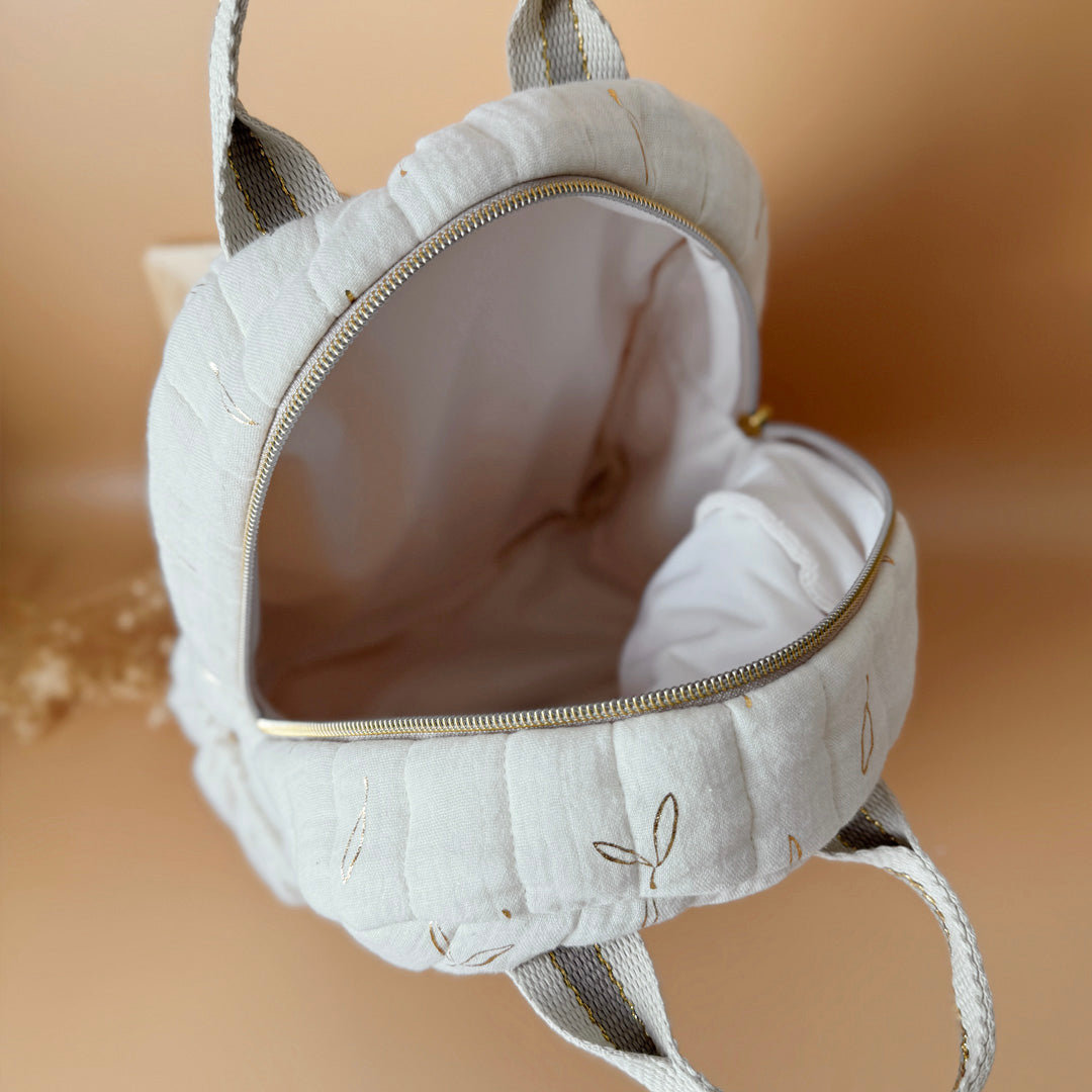 Voici notre tout nouveau sac à dos maternelle, pensé et confectionné en France pour accompagner vos tout-petits dans leurs premières journées d'école. Ce modèle délicat est réalisé en gaze de coton matelassée écrue, ornée de petites feuilles dorées qui lui donnent une allure douce et poétique. La grande particularité de ce sac ? Il est personnalisé avec le prénom de votre enfant, brodé à la main en fil doré sur la poche avant. Un détail unique, raffiné, et tellement précieux pour marquer les affaires de vot