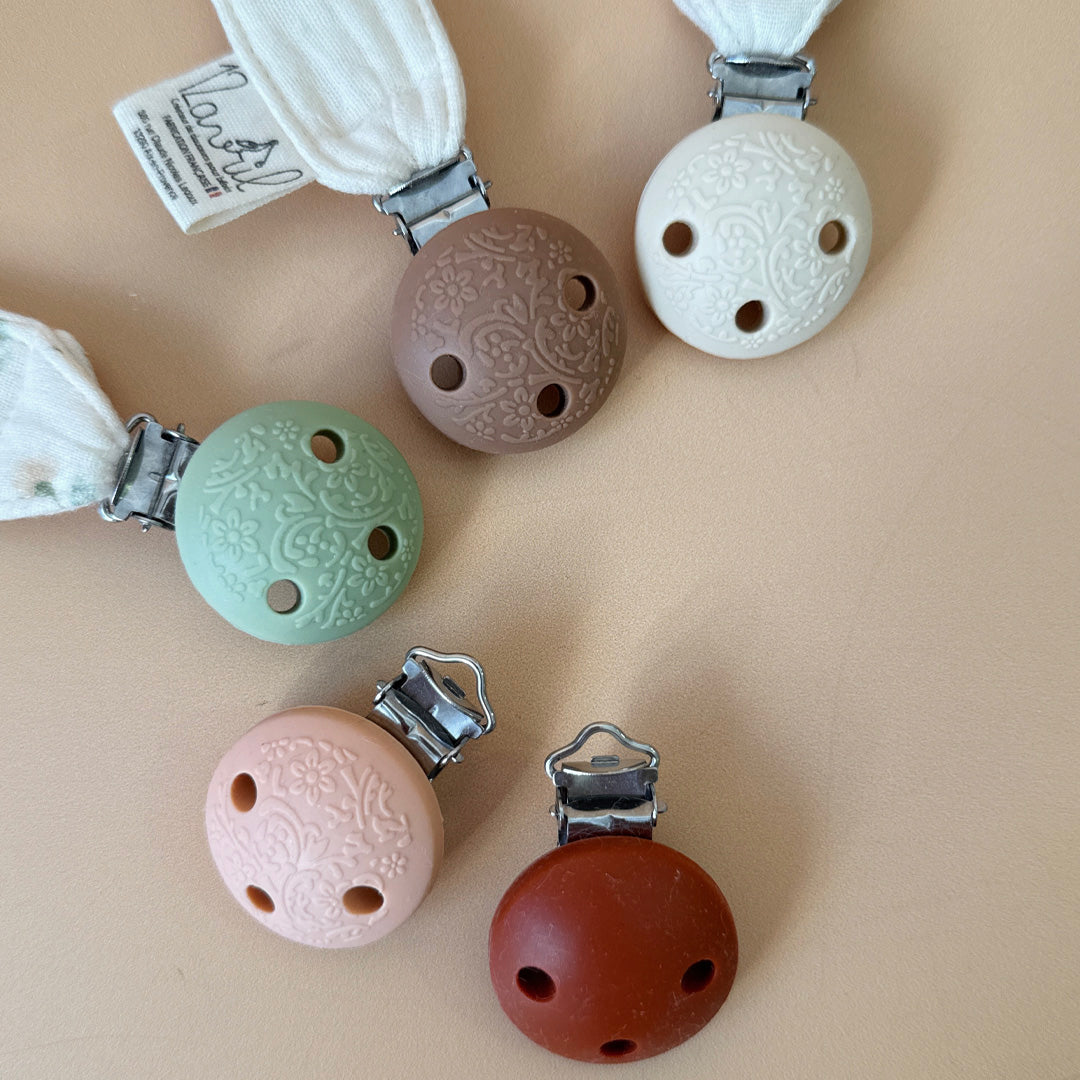 Élégante, douce et sécurisée, notre attache tétine en gaze de coton  accompagne bébé au quotidien tout en ajoutant une touche délicate à sa tenue. Chaque modèle est personnalisable avec le prénom de bébé, soigneusement brodé à la main, pour créer un accessoire unique et plein de sens. Dotée d’un lien doré raffiné pour fixer la tétine et d’une pince ronde en silicone embossé, elle allie esthétique et praticité.