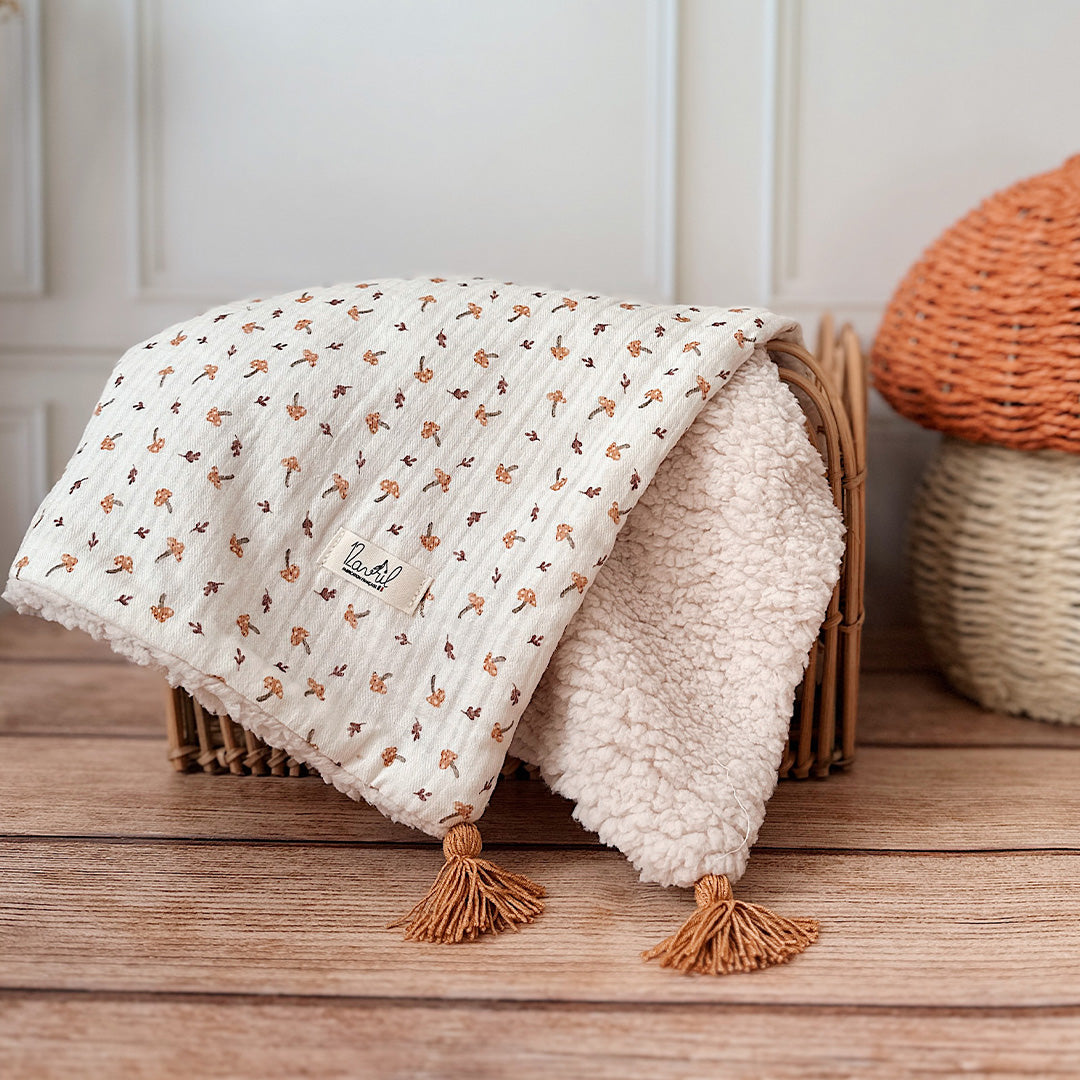 Découvrez la couverture pour bébé idéale pour apporter chaleur et douceur au quotidien de votre tout-petit ! Confectionnée à la main en France, cette couverture unique se compose d’une face au motif champignon enchanteur et d’une face en fausse fourrure sherpa beige extra douce, assurant confort et style. Pour un charme supplémentaire, quatre pompons couleur cassonade décorent élégamment chaque coin de la couverture. Et pour une touche encore plus personnelle, elle peut être brodée avec le prénom de votre b