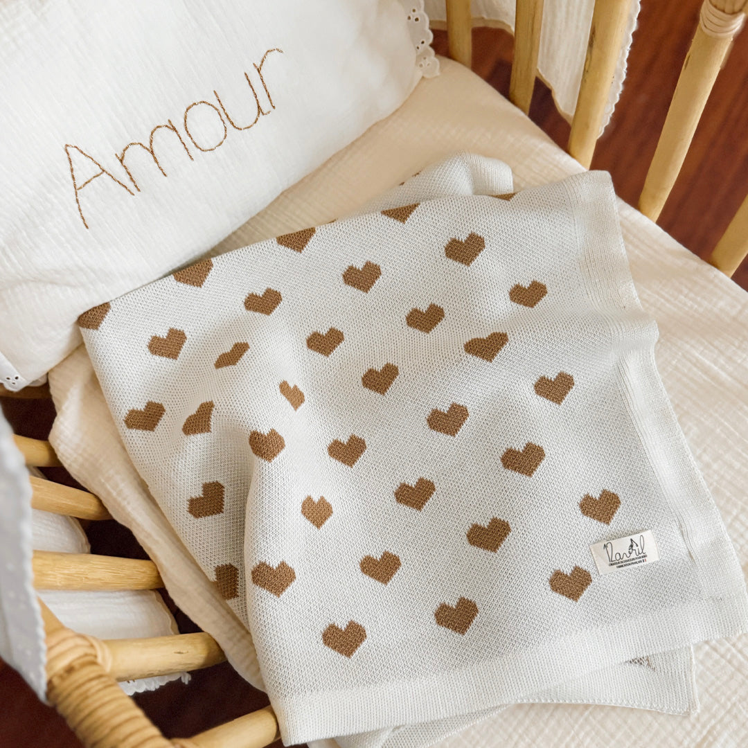 La couverture de naissance 12avril est bien plus qu’un simple accessoire : c’est un cocon de douceur et de chaleur, imaginé et tricoté avec soin en France, au cœur de la région roannaise, réputée pour son savoir-faire textile. Avec son motif all-over de petits cœurs biscuit délicatement posés sur un fond écru, elle séduit au premier regard par son esthétique tendre et intemporelle. Cette couverture est pensée pour réchauffer bébé tout en apportant une touche élégante et raffinée à sa chambre ou à vos sortie