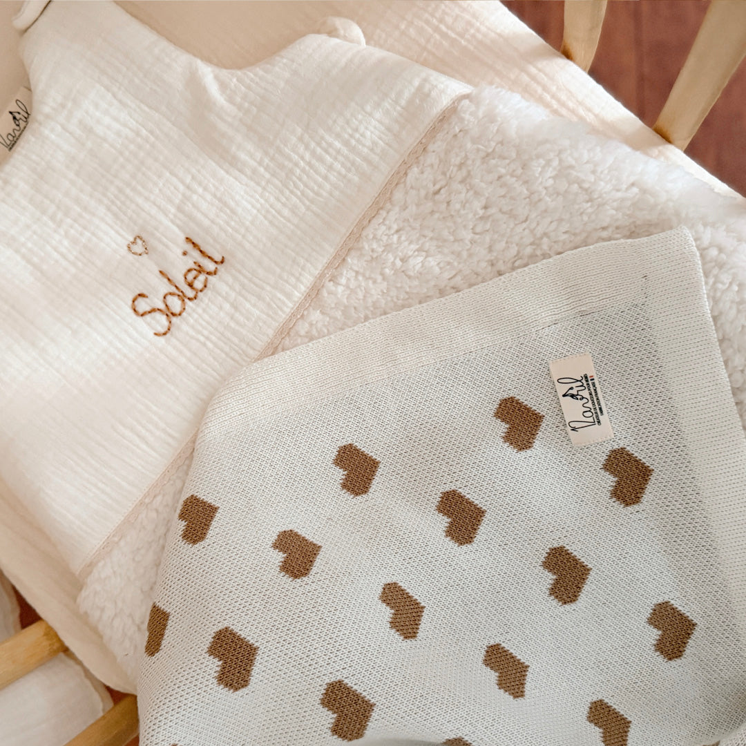La couverture de naissance 12avril est bien plus qu’un simple accessoire : c’est un cocon de douceur et de chaleur, imaginé et tricoté avec soin en France, au cœur de la région roannaise, réputée pour son savoir-faire textile. Avec son motif all-over de petits cœurs biscuit délicatement posés sur un fond écru, elle séduit au premier regard par son esthétique tendre et intemporelle. Cette couverture est pensée pour réchauffer bébé tout en apportant une touche élégante et raffinée à sa chambre ou à vos sortie