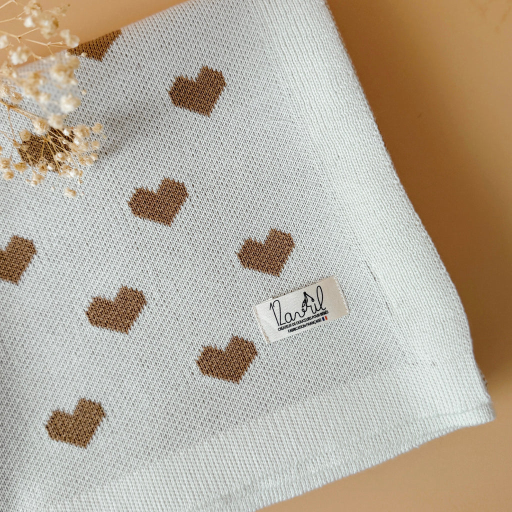La couverture de naissance 12avril est bien plus qu’un simple accessoire : c’est un cocon de douceur et de chaleur, imaginé et tricoté avec soin en France, au cœur de la région roannaise, réputée pour son savoir-faire textile. Avec son motif all-over de petits cœurs biscuit délicatement posés sur un fond écru, elle séduit au premier regard par son esthétique tendre et intemporelle. Cette couverture est pensée pour réchauffer bébé tout en apportant une touche élégante et raffinée à sa chambre ou à vos sortie
