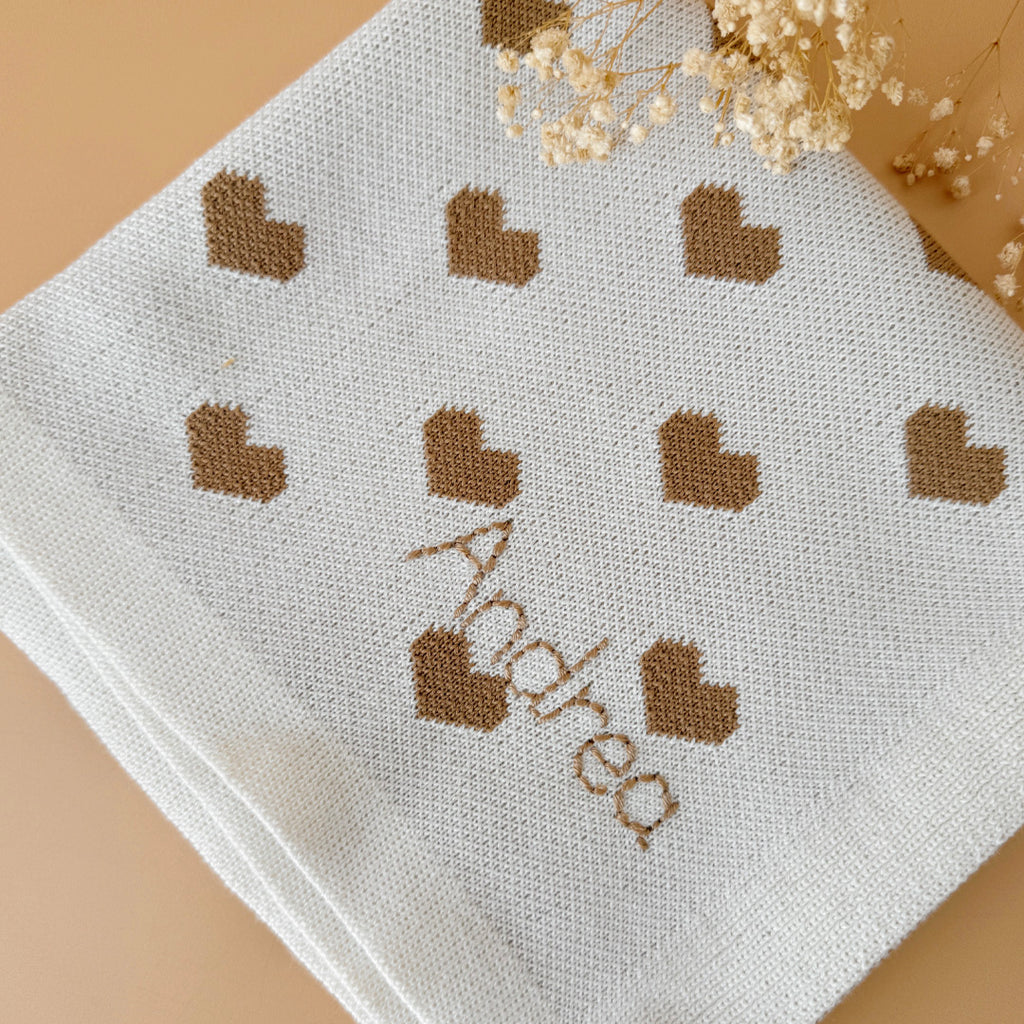 La couverture de naissance 12avril est bien plus qu’un simple accessoire : c’est un cocon de douceur et de chaleur, imaginé et tricoté avec soin en France, au cœur de la région roannaise, réputée pour son savoir-faire textile. Avec son motif all-over de petits cœurs biscuit délicatement posés sur un fond écru, elle séduit au premier regard par son esthétique tendre et intemporelle. Cette couverture est pensée pour réchauffer bébé tout en apportant une touche élégante et raffinée à sa chambre ou à vos sortie