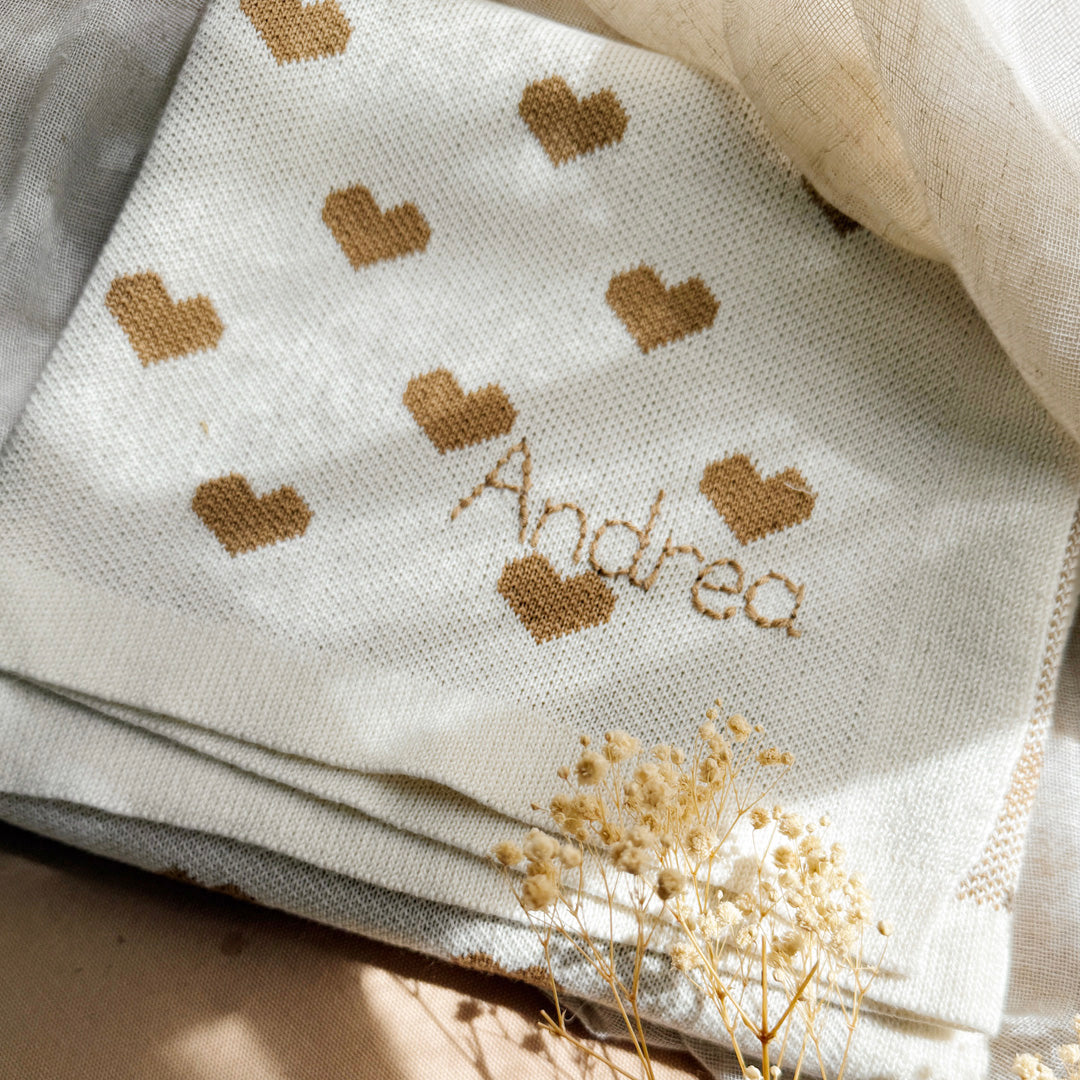 La couverture de naissance 12avril est bien plus qu’un simple accessoire : c’est un cocon de douceur et de chaleur, imaginé et tricoté avec soin en France, au cœur de la région roannaise, réputée pour son savoir-faire textile. Avec son motif all-over de petits cœurs biscuit délicatement posés sur un fond écru, elle séduit au premier regard par son esthétique tendre et intemporelle. Cette couverture est pensée pour réchauffer bébé tout en apportant une touche élégante et raffinée à sa chambre ou à vos sortie
