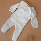 Offrez à votre bébé un premier vêtement doux, élégant et entièrement fabriqué en France avec cet adorable ensemble de naissance en maille blanche. Composé d'une brassière au col en dentelle de coton et d'un pantalon assorti, cet ensemble est tricoté avec soin dans une maille jersey, un point traditionnel qui lui confère un relief raffiné et un toucher délicatement texturé. La brassière croisée s'attache facilement grâce à de petits boutons  pour habiller bébé tout en douceur et sans effort. Le pantalon à ta