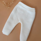 Offrez à votre bébé un premier vêtement doux, élégant et entièrement fabriqué en France avec cet adorable ensemble de naissance en maille blanche. Composé d'une brassière au col en dentelle de coton et d'un pantalon assorti, cet ensemble est tricoté avec soin dans une maille jersey, un point traditionnel qui lui confère un relief raffiné et un toucher délicatement texturé. La brassière croisée s'attache facilement grâce à de petits boutons  pour habiller bébé tout en douceur et sans effort. Le pantalon à ta
