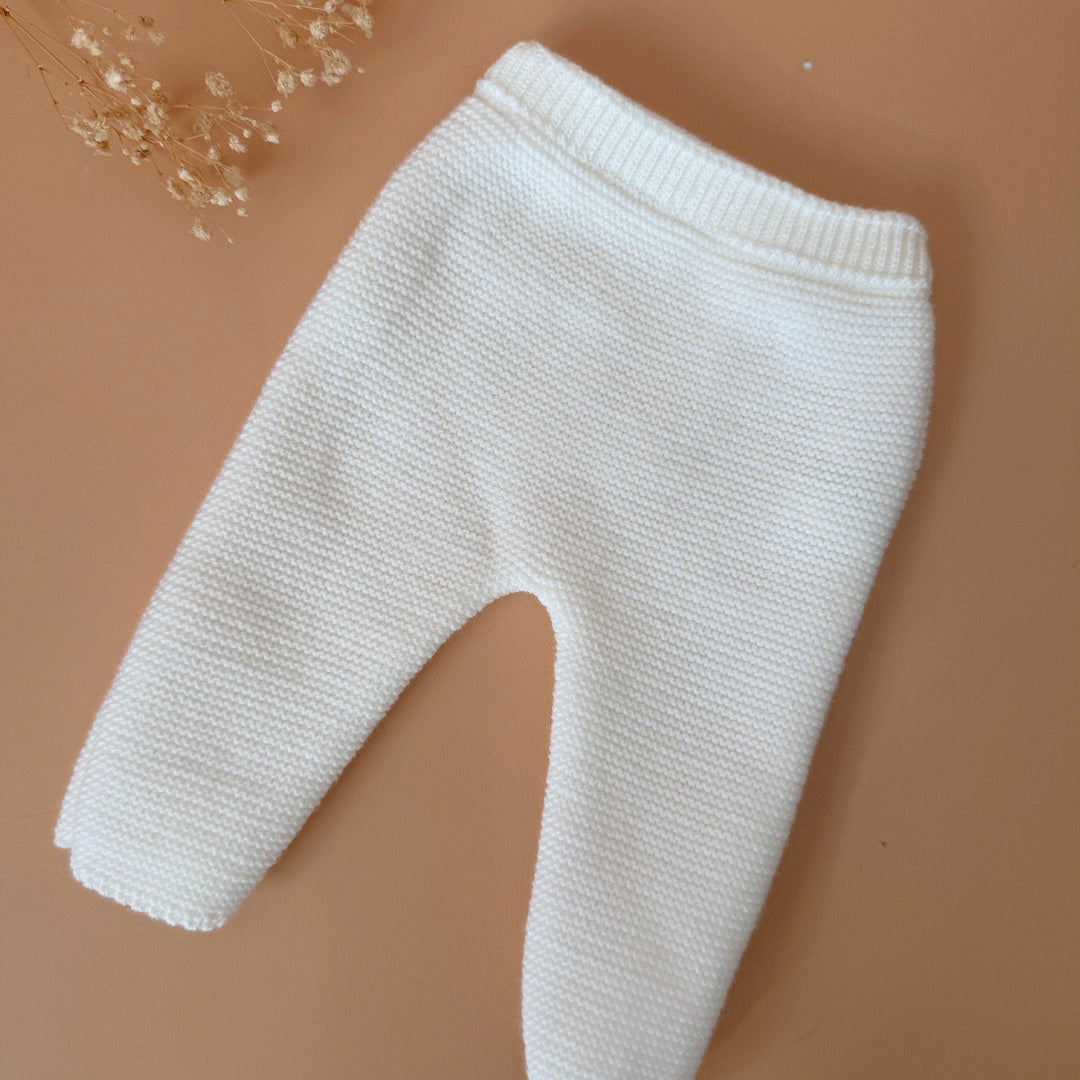 Offrez à votre bébé un premier vêtement doux, élégant et entièrement fabriqué en France avec cet adorable ensemble de naissance en maille blanche. Composé d'une brassière au col en dentelle de coton et d'un pantalon assorti, cet ensemble est tricoté avec soin dans une maille jersey, un point traditionnel qui lui confère un relief raffiné et un toucher délicatement texturé. La brassière croisée s'attache facilement grâce à de petits boutons  pour habiller bébé tout en douceur et sans effort. Le pantalon à ta