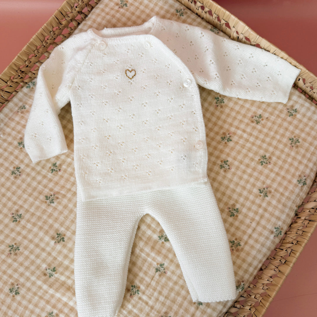 Offrez à votre bébé un premier vêtement doux, élégant et entièrement fabriqué en France avec cet adorable ensemble de naissance en maille blanche. Composé d'une brassière au col en dentelle de coton et d'un pantalon assorti, cet ensemble est tricoté avec soin dans une maille jersey, un point traditionnel qui lui confère un relief raffiné et un toucher délicatement texturé. La brassière croisée s'attache facilement grâce à de petits boutons  pour habiller bébé tout en douceur et sans effort. Le pantalon à ta