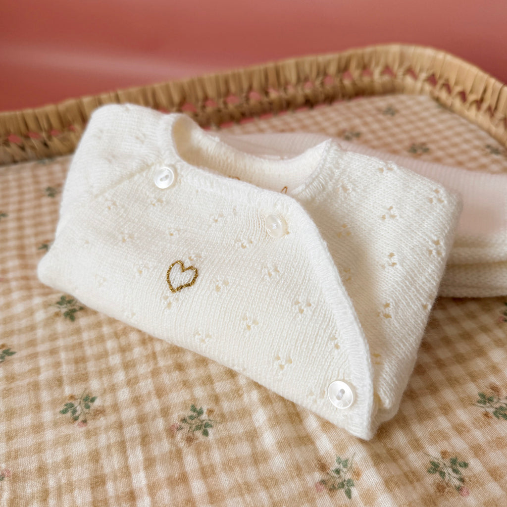 Offrez à votre bébé un premier vêtement doux, élégant et entièrement fabriqué en France avec cet adorable ensemble de naissance en maille blanche. Composé d'une brassière au col en dentelle de coton et d'un pantalon assorti, cet ensemble est tricoté avec soin dans une maille jersey, un point traditionnel qui lui confère un relief raffiné et un toucher délicatement texturé. La brassière croisée s'attache facilement grâce à de petits boutons  pour habiller bébé tout en douceur et sans effort. Le pantalon à ta