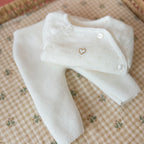 Offrez à votre bébé un premier vêtement doux, élégant et entièrement fabriqué en France avec cet adorable ensemble de naissance en maille blanche. Composé d'une brassière au col en dentelle de coton et d'un pantalon assorti, cet ensemble est tricoté avec soin dans une maille jersey, un point traditionnel qui lui confère un relief raffiné et un toucher délicatement texturé. La brassière croisée s'attache facilement grâce à de petits boutons  pour habiller bébé tout en douceur et sans effort. Le pantalon à ta
