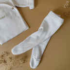 Offrez à votre bébé un premier vêtement doux, élégant et entièrement fabriqué en France avec cet adorable ensemble de naissance en maille blanche. Composé d'une brassière croisée et d'un pantalon assorti, cet ensemble est tricoté avec soin dans une maille jersey, un point traditionnel qui lui confère un relief raffiné et un toucher délicatement texturé. La brassière croisée s'attache facilement grâce à de petits boutons coloris bois, pour habiller bébé tout en douceur et sans effort. Le pantalon à taille él
