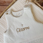 Cette gigoteuse pour bébé, confectionnée avec soin, est le choix idéal pour garder bébé au chaud durant l’hiver. Fabriquée en fausse fourrure type sherpa et en gaze de coton écrue, elle allie douceur et élégance. Son design raffiné, avec un empiècement en gaze de coton orné de délicate dentelle en broderie anglaise, en fait un accessoire de choix pour un sommeil cosy et stylé. Personnalisez la gigoteuse de bébé Vous avez la possibilité de personnaliser la gigoteuse avec le prénom ou le surnom de bébé, brodé