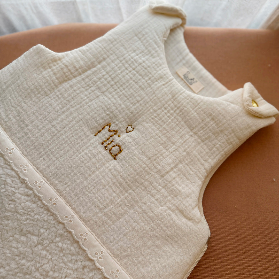 Cette gigoteuse pour bébé, confectionnée avec soin, est le choix idéal pour garder bébé au chaud durant l’hiver. Fabriquée en fausse fourrure type sherpa et en gaze de coton écrue, elle allie douceur et élégance. Son design raffiné, avec un empiècement en gaze de coton orné de délicate dentelle en broderie anglaise, en fait un accessoire de choix pour un sommeil cosy et stylé. Personnalisez la gigoteuse de bébé Vous avez la possibilité de personnaliser la gigoteuse avec le prénom ou le surnom de bébé, brodé