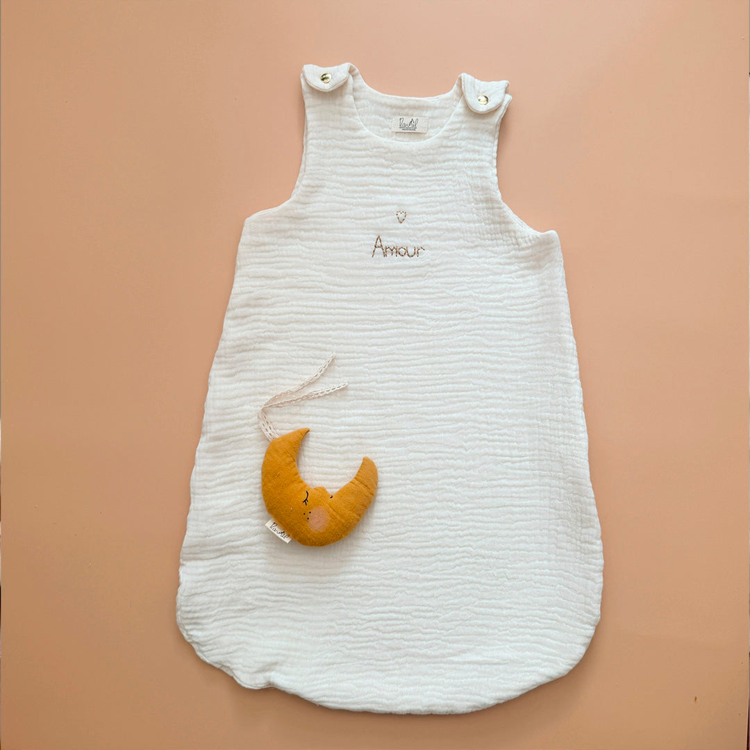 Gigoteuse d'Été en Triple Gaze de Coton Bio – Personnalisable Offrez à votre bébé un confort inégalé pendant les nuits d'été avec cette magnifique gigoteuse confectionnée dans une triple gaze de coton biologique certifiée Oeko-Tex, une matière d'exception bien plus douce et respirante que la traditionnelle double gaze. Sa texture gaufrée naturelle apporte douceur, légèreté et élégance. Disponible en coloris écru, cette gigoteuse est personnalisable au prénom de votre enfant, délicatement brodé sous un petit
