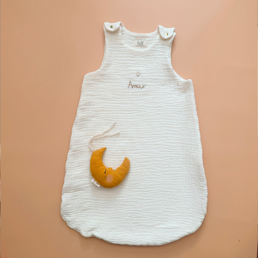 Gigoteuse d'Été en Triple Gaze de Coton Bio – Personnalisable Offrez à votre bébé un confort inégalé pendant les nuits d'été avec cette magnifique gigoteuse confectionnée dans une triple gaze de coton biologique certifiée Oeko-Tex, une matière d'exception bien plus douce et respirante que la traditionnelle double gaze. Sa texture gaufrée naturelle apporte douceur, légèreté et élégance. Disponible en coloris écru, cette gigoteuse est personnalisable au prénom de votre enfant, délicatement brodé sous un petit