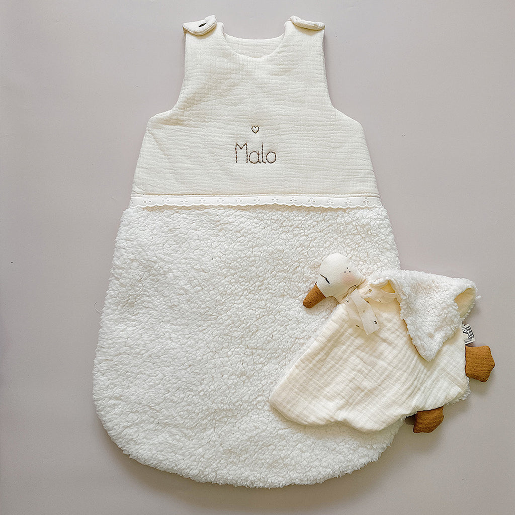 Cette gigoteuse pour bébé, confectionnée avec soin, est le choix idéal pour garder bébé au chaud durant l’hiver. Fabriquée en fausse fourrure type sherpa et en gaze de coton écrue, elle allie douceur et élégance. Son design raffiné, avec un empiècement en gaze de coton orné de délicate dentelle en broderie anglaise, en fait un accessoire de choix pour un sommeil cosy et stylé. Personnalisez la gigoteuse de bébé Vous avez la possibilité de personnaliser la gigoteuse avec le prénom ou le surnom de bébé, brodé