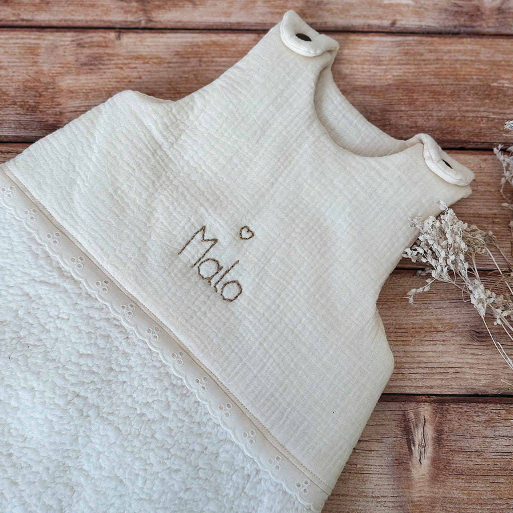 Cette gigoteuse pour bébé, confectionnée avec soin, est le choix idéal pour garder bébé au chaud durant l’hiver. Fabriquée en fausse fourrure type sherpa et en gaze de coton écrue, elle allie douceur et élégance. Son design raffiné, avec un empiècement en gaze de coton orné de délicate dentelle en broderie anglaise, en fait un accessoire de choix pour un sommeil cosy et stylé. Personnalisez la gigoteuse de bébé Vous avez la possibilité de personnaliser la gigoteuse avec le prénom ou le surnom de bébé, brodé