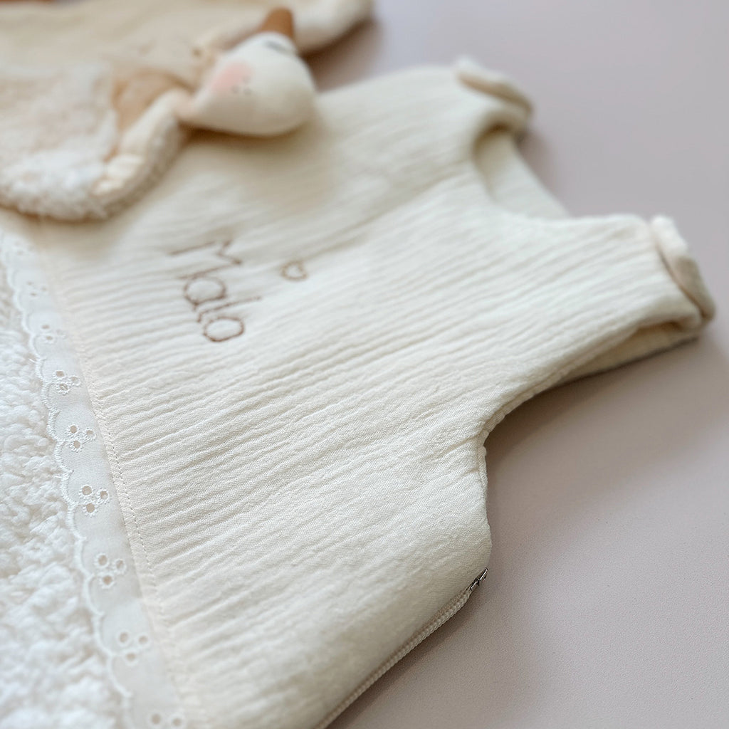 Cette gigoteuse pour bébé, confectionnée avec soin, est le choix idéal pour garder bébé au chaud durant l’hiver. Fabriquée en fausse fourrure type sherpa et en gaze de coton écrue, elle allie douceur et élégance. Son design raffiné, avec un empiècement en gaze de coton orné de délicate dentelle en broderie anglaise, en fait un accessoire de choix pour un sommeil cosy et stylé. Personnalisez la gigoteuse de bébé Vous avez la possibilité de personnaliser la gigoteuse avec le prénom ou le surnom de bébé, brodé