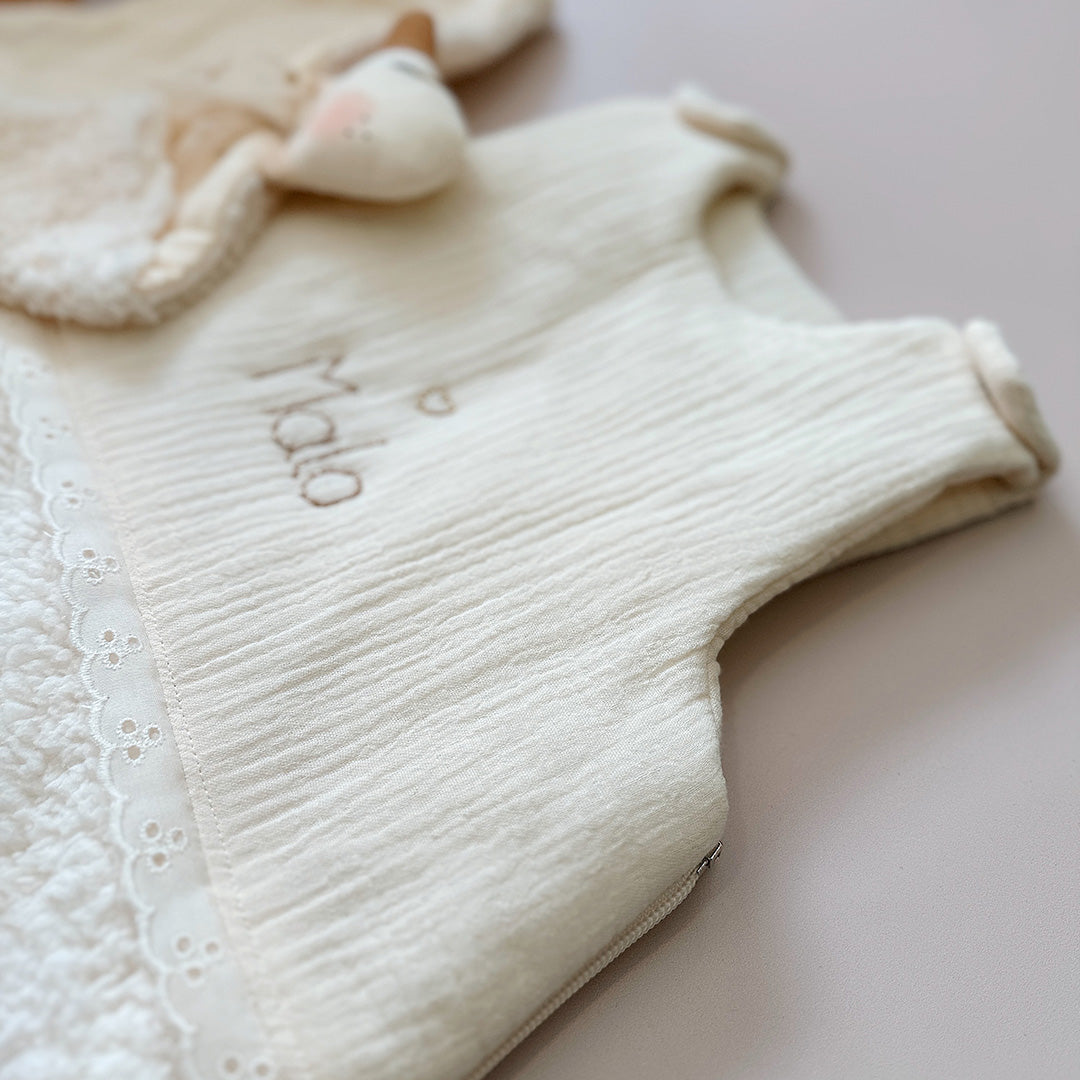 Cette gigoteuse pour bébé, confectionnée avec soin, est le choix idéal pour garder bébé au chaud durant l’hiver. Fabriquée en fausse fourrure type sherpa et en gaze de coton écrue, elle allie douceur et élégance. Son design raffiné, avec un empiècement en gaze de coton orné de délicate dentelle en broderie anglaise, en fait un accessoire de choix pour un sommeil cosy et stylé. Personnalisez la gigoteuse de bébé Vous avez la possibilité de personnaliser la gigoteuse avec le prénom ou le surnom de bébé, brodé