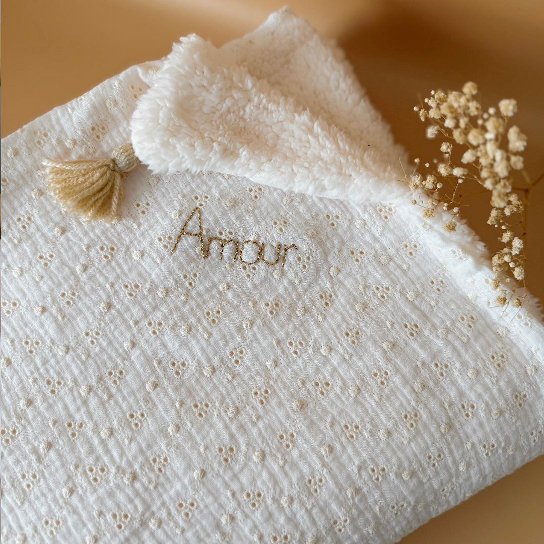 Apportez chaleur, tendresse et raffinement à votre quotidien avec cette magnifique couverture personnalisable, confectionnée avec soin en France. Un véritable cocon de douceur, pensé pour envelopper les petits et les grands dans un nuage de confort. Un textile d’exception, doux et élégant Cette grande couverture de 105 x 130 cm marie subtilement deux matières nobles et douces : Une face en gaze de coton brodée, inspirée de la broderie anglaise, légère et respirante, aux motifs floraux délicats qui évoquent 