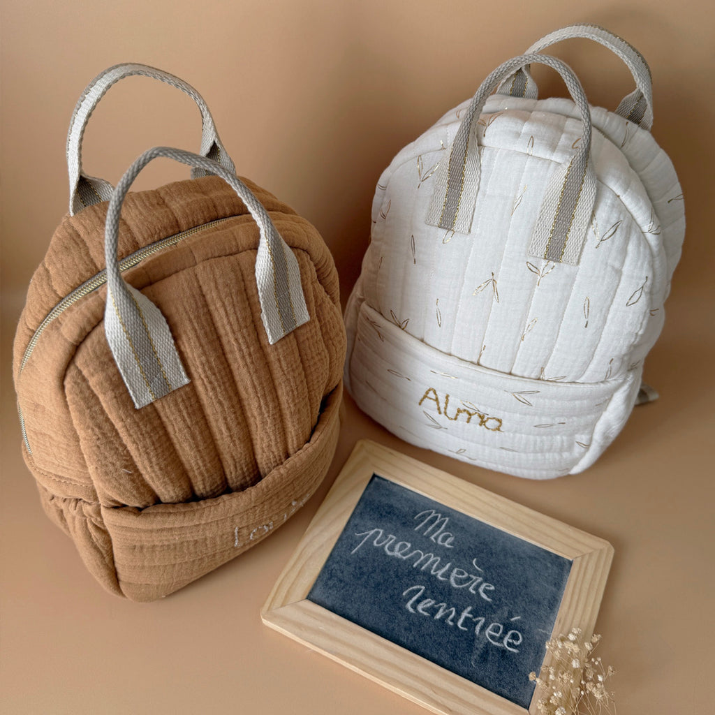 Découvrez notre sac à dos maternelle personnalisé, confectionné avec soin en France pour accompagner les tout-petits dans leurs premières aventures à l’école. Ce modèle est réalisé en gaze de coton matelassé, douce et respirante, dans un joli coloris biscuit chaleureux et intemporel. Ce sac se distingue par sa personnalisation brodée à la main : le prénom de l’enfant est délicatement inscrit sur la poche avant avec un fil doré clair ou argenté, pour un rendu raffiné et unique. Une attention particulière qui