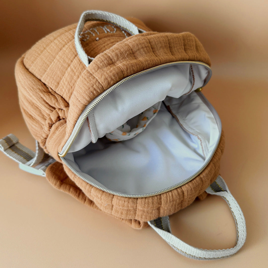 Découvrez notre sac à dos maternelle personnalisé, confectionné avec soin en France pour accompagner les tout-petits dans leurs premières aventures à l’école. Ce modèle est réalisé en gaze de coton matelassé, douce et respirante, dans un joli coloris biscuit chaleureux et intemporel. Ce sac se distingue par sa personnalisation brodée à la main : le prénom de l’enfant est délicatement inscrit sur la poche avant avec un fil doré clair ou argenté, pour un rendu raffiné et unique. Une attention particulière qui