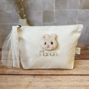 Cette jolie trousse de toilette deviendra vite l' indispensable de bébé à glisser partout ! Elle est réalisée en 100% toile de coton biologique. Une jolie petite tête de lapin en fourrure est délicatement cousue , puis nous brodons le prénom que vous désirez avec un fil de lurex doré. Le tout est contrecollé à l'intérieur pour un maximum de solidité. Son ouverture zippée est agrémentée par un lien en tulle à pois doré, ce qui facilitera l'ouverture.