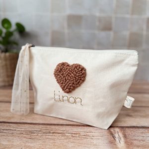 Cette jolie trousse de toilette deviendra vite l' indispensable de bébé ou bien pour maman à glisser partout ! Elle est réalisée en 100% toile de coton biologique. Nous réalisons ensuite, une broderie main au motif  cœur en laine de couleur noisette, puis nous brodons le prénom que vous désirez avec un fil de lurex doré. Son ouverture zippée est agrémentée par un lien en tulle à pois doré, ce qui facilitera son ouverture.