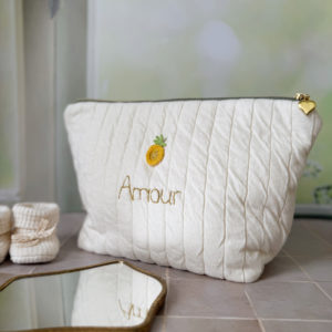 Apportez une touche de tendresse à vos accessoires avec cette trousse de toilette matelassée en jersey de coton, entièrement confectionnée en France. Pensée pour les mamans, les enfants ou tout simplement pour se faire plaisir, cette trousse incarne à la fois le charme artisanal et la fonctionnalité. Son tissu matelassé lui confère une allure douce et moelleuse, parfaite pour y glisser les essentiels de toilette ou les petits trésors du quotidien. Ce qui la rend unique ? Son joli petit ananas jaune mordoré cousu sur le devant, associée à une broderie  personnalisée au prénom de votre choix. Chaque trousse est brodée à la main avec soin, rendant chaque pièce unique et affectueuse. Idéale comme cadeau de naissance, de babyshower, ou pour toute occasion où l’on veut faire plaisir avec du fait-main de qualité. Fièrement fabriquée en France, cette trousse de toilette est le fruit d'un savoir-faire artisanal et d'une attention particulière aux détails. Zoom sur le petit curseur de la fermeture à glissière !