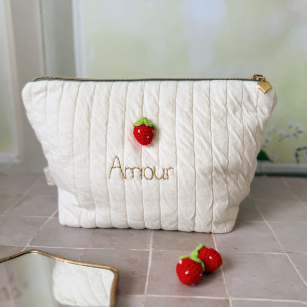 Apportez une touche de tendresse à vos accessoires avec cette trousse de toilette matelassée en jersey de coton, entièrement confectionnée en France. Pensée pour les mamans, les enfants ou tout simplement pour se faire plaisir, cette trousse incarne à la fois le charme artisanal et la fonctionnalité. Son tissu matelassé lui confère une allure douce et moelleuse, parfaite pour y glisser les essentiels de toilette ou les petits trésors du quotidien. Ce qui la rend unique ? Sa jolie fraise en crochet rouge cousue sur le devant, associée à une broderie dorée personnalisée au prénom de votre choix. Chaque trousse est brodée à la main avec soin, rendant chaque pièce unique et affectueuse. Idéale comme cadeau de naissance, de babyshower, ou pour toute occasion où l’on veut faire plaisir avec du fait-main de qualité.