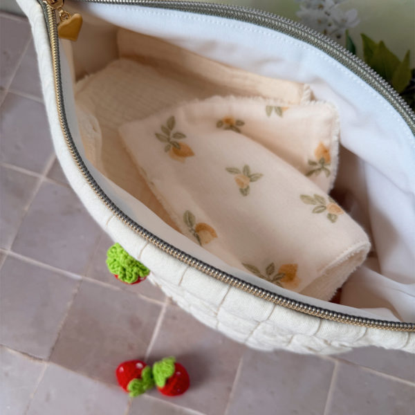 Apportez une touche de tendresse à vos accessoires avec cette trousse de toilette matelassée en jersey de coton, entièrement confectionnée en France. Pensée pour les mamans, les enfants ou tout simplement pour se faire plaisir, cette trousse incarne à la fois le charme artisanal et la fonctionnalité. Son tissu matelassé lui confère une allure douce et moelleuse, parfaite pour y glisser les essentiels de toilette ou les petits trésors du quotidien. Ce qui la rend unique ? Sa jolie fraise en crochet rouge cousue sur le devant, associée à une broderie dorée personnalisée au prénom de votre choix. Chaque trousse est brodée à la main avec soin, rendant chaque pièce unique et affectueuse. Idéale comme cadeau de naissance, de babyshower, ou pour toute occasion où l’on veut faire plaisir avec du fait-main de qualité.