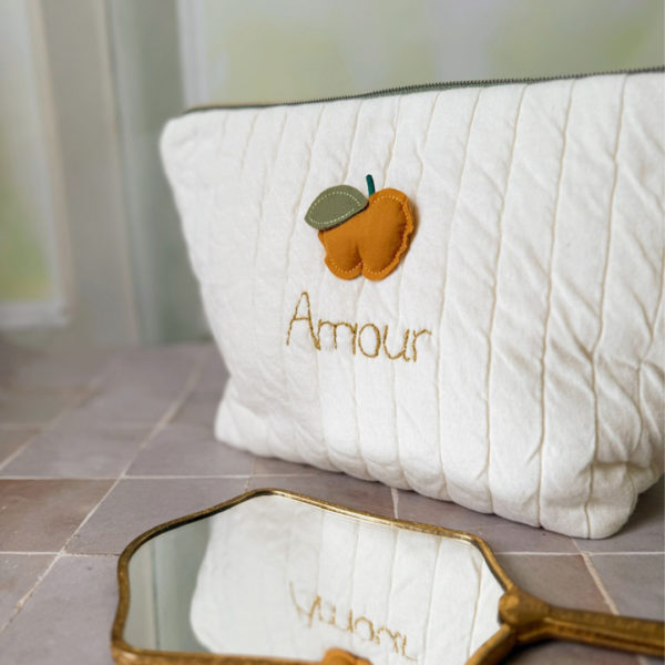 Apportez une touche de tendresse à vos accessoires avec cette trousse de toilette matelassée en jersey de coton, entièrement confectionnée en France. Pensée pour les mamans, les enfants ou tout simplement pour se faire plaisir, cette trousse incarne à la fois le charme artisanal et la fonctionnalité. Son tissu matelassé lui confère une allure douce et moelleuse, parfaite pour y glisser les essentiels de toilette ou les petits trésors du quotidien. Ce qui la rend unique ? Sa jolie pomme en relief appliquée cousue sur le devant, associée à une broderie dorée personnalisée au prénom de votre choix. Chaque trousse est brodée à la main avec soin, rendant chaque pièce unique et affectueuse. Idéale comme cadeau de naissance, de babyshower, ou pour toute occasion où l’on veut faire plaisir avec du fait-main de qualité. Fièrement fabriquée en France, cette trousse de toilette est le fruit d'un savoir-faire artisanal et d'une attention particulière aux détails. Zoom sur le petit curseur de la fermeture à glissière !