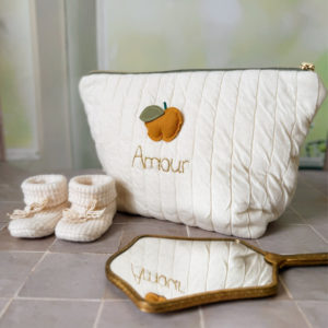 Apportez une touche de tendresse à vos accessoires avec cette trousse de toilette matelassée en jersey de coton, entièrement confectionnée en France. Pensée pour les mamans, les enfants ou tout simplement pour se faire plaisir, cette trousse incarne à la fois le charme artisanal et la fonctionnalité. Son tissu matelassé lui confère une allure douce et moelleuse, parfaite pour y glisser les essentiels de toilette ou les petits trésors du quotidien. Ce qui la rend unique ? Sa jolie pomme en relief appliquée cousue sur le devant, associée à une broderie dorée personnalisée au prénom de votre choix. Chaque trousse est brodée à la main avec soin, rendant chaque pièce unique et affectueuse. Idéale comme cadeau de naissance, de babyshower, ou pour toute occasion où l’on veut faire plaisir avec du fait-main de qualité. Fièrement fabriquée en France, cette trousse de toilette est le fruit d'un savoir-faire artisanal et d'une attention particulière aux détails. Zoom sur le petit curseur de la fermeture à glissière !