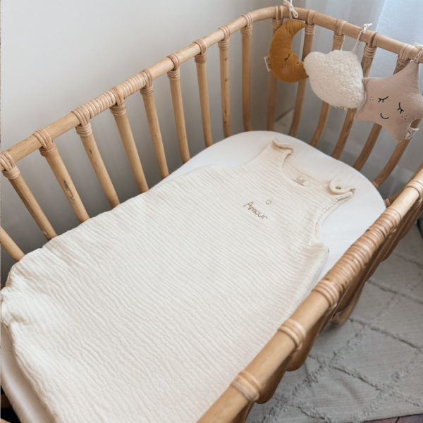 Gigoteuse d'Été en Triple Gaze de Coton Bio – Personnalisable Offrez à votre bébé un confort inégalé pendant les nuits d'été avec cette magnifique gigoteuse confectionnée dans une triple gaze de coton biologique certifiée Oeko-Tex, une matière d'exception bien plus douce et respirante que la traditionnelle double gaze. Sa texture gaufrée naturelle apporte douceur, légèreté et élégance. Disponible en coloris écru, cette gigoteuse est personnalisable au prénom de votre enfant, délicatement brodé sous un petit cœur doré au centre, ajoutant une touche poétique et unique. Conçue pour faciliter le quotidien des parents, elle s'ouvre aisément grâce à deux pressions dorées aux épaules et une grande fermeture à glissière latérale, permettant un habillage simple et rapide, même lorsque bébé dort. Un véritable cocon de tendresse, pensé pour le bien-être des tout-petits et la tranquillité des grands.