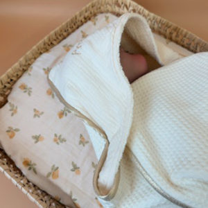 Offrez à votre nouveau-né une sortie de bain tout en douceur avec notre cape de bain de naissance en nid d’éponge, confectionnée en coton 100% naturel. Cette cape innovante associe deux textures complémentaires : L’éponge ultra absorbante, idéale pour sécher bébé rapidement, Et le nid d’abeille moelleux, parfait pour envelopper délicatement sa peau fragile. Sa forme carrée de 70 x 70 cm est spécialement pensée pour les tout-petits. Elle épouse parfaitement la taille de bébé pendant ses premiers mois, sans excès de tissu, et permet une manipulation facile après le bain. La capuche en gaze de coton, douce et respirante, protège sa petite tête. En option, vous pouvez la faire broder au prénom de votre bébé, pour un souvenir unique et plein d’émotion. Une broderie délicate accompagnée d’un petit cœur doré ajoute une touche de tendresse et d’élégance à l’ensemble. Chaque cape est gansée d’un biais beige doré, pour une finition soignée et raffinée qui en fait un véritable objet de naissance haut de gamme.