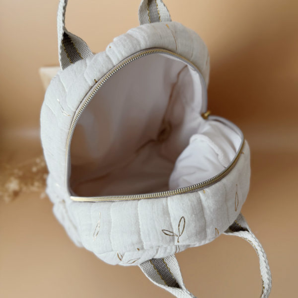 Voici notre tout nouveau sac à dos maternelle, pensé et confectionné en France pour accompagner vos tout-petits dans leurs premières journées d'école. Ce modèle délicat est réalisé en gaze de coton matelassée écrue, ornée de petites feuilles dorées qui lui donnent une allure douce et poétique. La grande particularité de ce sac ? Il est personnalisé avec le prénom de votre enfant, brodé à la main en fil doré sur la poche avant. Un détail unique, raffiné, et tellement précieux pour marquer les affaires de votre petit. L’intérieur du sac est entièrement doublé avec un tissu imperméable, parfait pour protéger son contenu contre les petits accidents ou les surprises météo. Son ouverture zippée large a été pensée pour que les enfants puissent l’utiliser en toute autonomie. Il comporte trois poches intelligentes, dont deux latérales élastiquées idéales pour glisser une gourde, un doudou ou les trésors ramassés à la récréation. Côté confort, rien n’a été laissé au hasard : bretelles matelassées réglables et ajustables pour un bon maintien sans tirer sur les épaules, et deux anses solides pour une prise en main facile par les petits ou les adultes. C'est plus qu’un sac à dos : c’est un vrai compagnon de rentrée, beau, pratique, doux pour le dos, et surtout unique grâce à sa personnalisation.