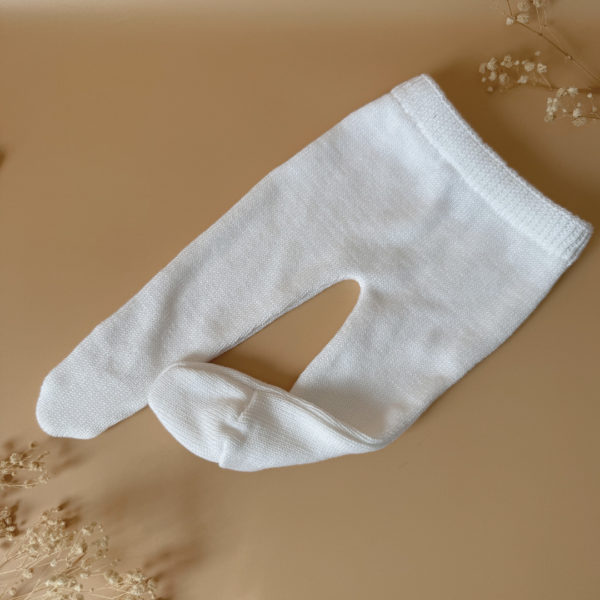 Offrez à votre bébé un premier vêtement doux, élégant et entièrement fabriqué en France avec cet adorable ensemble de naissance en maille blanche. Composé d'une brassière croisée et d'un pantalon assorti, cet ensemble est tricoté avec soin dans une maille jersey, un point traditionnel qui lui confère un relief raffiné et un toucher délicatement texturé. La brassière croisée s'attache facilement grâce à de petits boutons coloris bois, pour habiller bébé tout en douceur et sans effort. Le pantalon à taille élastiquée et à pieds  assure un confort optimal et un bon maintien, sans comprimer le ventre fragile des nouveau-nés. Ce modèle est intégralement tricoté en France, en collaboration avec un atelier partenaire reconnu pour son savoir-faire en maille fine pour bébé. Une attention toute particulière est portée à la qualité des finitions, pour un rendu chic, intemporel et parfaitement adapté à la peau des tout-petits. Et pour rendre ce cadeau de naissance encore plus unique, vous pouvez choisir de personnaliser la brassière avec une broderie faite main, directement au centre du vêtement. Que ce soit le prénom du bébé ou un petit mot doux, chaque pièce devient ainsi un souvenir précieux, plein d’émotion.