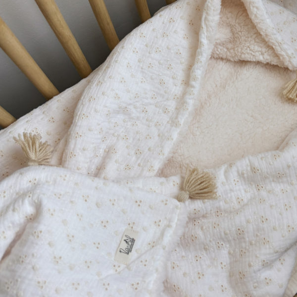 Apportez chaleur, tendresse et raffinement à votre quotidien avec cette magnifique couverture personnalisable, confectionnée avec soin en France. Un véritable cocon de douceur, pensé pour envelopper les petits et les grands dans un nuage de confort. Un textile d’exception, doux et élégant Cette grande couverture de 105 x 130 cm marie subtilement deux matières nobles et douces : Une face en gaze de coton brodée, inspirée de la broderie anglaise, légère et respirante, aux motifs floraux délicats qui évoquent la tendresse de l’enfance. Une face en fausse fourrure sherpa, épaisse et ultra-douce, idéale pour réchauffer les journées fraîches ou les soirées d’hiver. Le tout assemblé avec amour dans un atelier français, pour un résultat à la fois esthétique, pratique et durable. Une couverture unique grâce à la personnalisation Pour rendre cette couverture vraiment unique, nous vous proposons une broderie à la main du prénom, d’un mot doux ou d’une petite phrase de votre choix (ex. : Amour, Petit trésor, Louise, Mon bébé d’hiver…). Chaque broderie est réalisée avec soin, dans une teinte douce et naturelle, parfaitement en harmonie avec la couverture. 👉 Cette option de personnalisation en fait un cadeau de naissance idéal, un souvenir précieux à conserver pour la vie.
