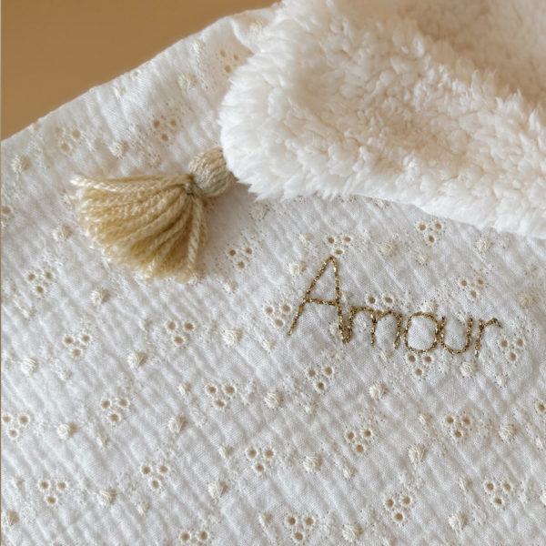 Apportez chaleur, tendresse et raffinement à votre quotidien avec cette magnifique couverture personnalisable, confectionnée avec soin en France. Un véritable cocon de douceur, pensé pour envelopper les petits et les grands dans un nuage de confort. Un textile d’exception, doux et élégant Cette grande couverture de 105 x 130 cm marie subtilement deux matières nobles et douces : Une face en gaze de coton brodée, inspirée de la broderie anglaise, légère et respirante, aux motifs floraux délicats qui évoquent la tendresse de l’enfance. Une face en fausse fourrure sherpa, épaisse et ultra-douce, idéale pour réchauffer les journées fraîches ou les soirées d’hiver. Le tout assemblé avec amour dans un atelier français, pour un résultat à la fois esthétique, pratique et durable. Une couverture unique grâce à la personnalisation Pour rendre cette couverture vraiment unique, nous vous proposons une broderie à la main du prénom, d’un mot doux ou d’une petite phrase de votre choix (ex. : Amour, Petit trésor, Louise, Mon bébé d’hiver…). Chaque broderie est réalisée avec soin, dans une teinte douce et naturelle, parfaitement en harmonie avec la couverture. 👉 Cette option de personnalisation en fait un cadeau de naissance idéal, un souvenir précieux à conserver pour la vie.