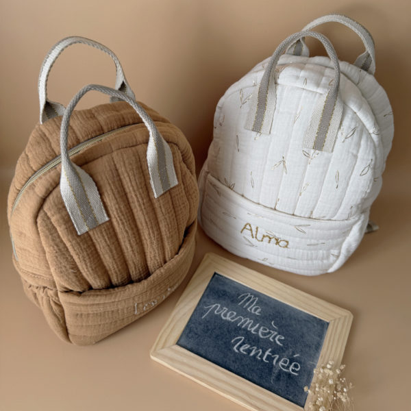 Découvrez notre sac à dos maternelle personnalisé, confectionné avec soin en France pour accompagner les tout-petits dans leurs premières aventures à l’école. Ce modèle est réalisé en gaze de coton matelassé, douce et respirante, dans un joli coloris biscuit chaleureux et intemporel. Ce sac se distingue par sa personnalisation brodée à la main : le prénom de l’enfant est délicatement inscrit sur la poche avant avec un fil doré clair ou argenté, pour un rendu raffiné et unique. Une attention particulière qui en fait un objet à la fois pratique et précieux. L’intérieur est entièrement doublé d’un tissu imperméable, afin de protéger le contenu des petits accidents du quotidien (gourdes mal fermées, goûter renversé, etc.). L’ouverture zippée est facile à manipuler par les petites mains, encourageant l’autonomie dès la petite section. Le sac est pensé pour être fonctionnel et ergonomique : il dispose de trois poches, dont deux latérales élastiquées idéales pour ranger une gourde, un doudou ou des petits jouets. Les bretelles matelassées et réglables assurent un confort optimal pour les épaules et le dos de votre enfant. Deux anses solides en sangle permettent de le porter facilement à la main. Ce sac à dos allie esthétique, confort et praticité, pour une rentrée maternelle sereine, tout en douceur.