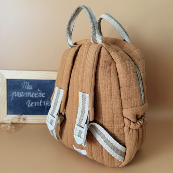 Découvrez notre sac à dos maternelle personnalisé, confectionné avec soin en France pour accompagner les tout-petits dans leurs premières aventures à l’école. Ce modèle est réalisé en gaze de coton matelassé, douce et respirante, dans un joli coloris biscuit chaleureux et intemporel. Ce sac se distingue par sa personnalisation brodée à la main : le prénom de l’enfant est délicatement inscrit sur la poche avant avec un fil doré clair ou argenté, pour un rendu raffiné et unique. Une attention particulière qui en fait un objet à la fois pratique et précieux. L’intérieur est entièrement doublé d’un tissu imperméable, afin de protéger le contenu des petits accidents du quotidien (gourdes mal fermées, goûter renversé, etc.). L’ouverture zippée est facile à manipuler par les petites mains, encourageant l’autonomie dès la petite section. Le sac est pensé pour être fonctionnel et ergonomique : il dispose de trois poches, dont deux latérales élastiquées idéales pour ranger une gourde, un doudou ou des petits jouets. Les bretelles matelassées et réglables assurent un confort optimal pour les épaules et le dos de votre enfant. Deux anses solides en sangle permettent de le porter facilement à la main. Ce sac à dos allie esthétique, confort et praticité, pour une rentrée maternelle sereine, tout en douceur.