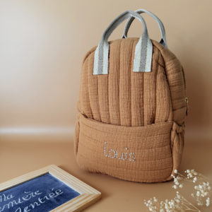 Découvrez notre sac à dos maternelle personnalisé, confectionné avec soin en France pour accompagner les tout-petits dans leurs premières aventures à l’école. Ce modèle est réalisé en gaze de coton matelassé, douce et respirante, dans un joli coloris biscuit chaleureux et intemporel. Ce sac se distingue par sa personnalisation brodée à la main : le prénom de l’enfant est délicatement inscrit sur la poche avant avec un fil doré clair ou argenté, pour un rendu raffiné et unique. Une attention particulière qui en fait un objet à la fois pratique et précieux. L’intérieur est entièrement doublé d’un tissu imperméable, afin de protéger le contenu des petits accidents du quotidien (gourdes mal fermées, goûter renversé, etc.). L’ouverture zippée est facile à manipuler par les petites mains, encourageant l’autonomie dès la petite section. Le sac est pensé pour être fonctionnel et ergonomique : il dispose de trois poches, dont deux latérales élastiquées idéales pour ranger une gourde, un doudou ou des petits jouets. Les bretelles matelassées et réglables assurent un confort optimal pour les épaules et le dos de votre enfant. Deux anses solides en sangle permettent de le porter facilement à la main. Ce sac à dos allie esthétique, confort et praticité, pour une rentrée maternelle sereine, tout en douceur.