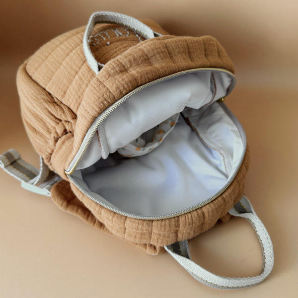 Découvrez notre sac à dos maternelle personnalisé, confectionné avec soin en France pour accompagner les tout-petits dans leurs premières aventures à l’école. Ce modèle est réalisé en gaze de coton matelassé, douce et respirante, dans un joli coloris biscuit chaleureux et intemporel. Ce sac se distingue par sa personnalisation brodée à la main : le prénom de l’enfant est délicatement inscrit sur la poche avant avec un fil doré clair ou argenté, pour un rendu raffiné et unique. Une attention particulière qui en fait un objet à la fois pratique et précieux. L’intérieur est entièrement doublé d’un tissu imperméable, afin de protéger le contenu des petits accidents du quotidien (gourdes mal fermées, goûter renversé, etc.). L’ouverture zippée est facile à manipuler par les petites mains, encourageant l’autonomie dès la petite section. Le sac est pensé pour être fonctionnel et ergonomique : il dispose de trois poches, dont deux latérales élastiquées idéales pour ranger une gourde, un doudou ou des petits jouets. Les bretelles matelassées et réglables assurent un confort optimal pour les épaules et le dos de votre enfant. Deux anses solides en sangle permettent de le porter facilement à la main. Ce sac à dos allie esthétique, confort et praticité, pour une rentrée maternelle sereine, tout en douceur.