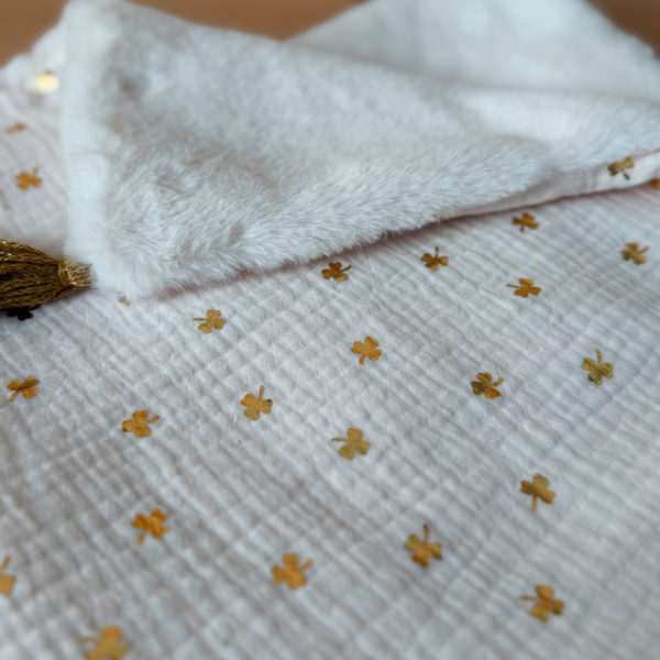 La couverture est une des pièces indispensable du trousseau de bébé. Parfaite en cadeau de naissance ou à s’offrir soit même, cette couverture chaude spéciale “bébés d’hiver”, vous accompagnera très longtemps dans vos moments câlins avec bébé. Les bébés d’hiver qui naissent pendant les mois les plus froids ont besoin d'être tenus bien au chaud à la sortie du ventre de maman. C'est pourquoi nous avons conçu cette couverture chaude spéciale “bébé d’hiver”. Dès son arrivée, bébé passe d'un environnement clos de 37°C à une température extérieure souvent très basse en hiver. C'est pour cela que nos couvertures d'hiver épaisses sont idéales pour réguler et maintenir une bonne température pour le corps de bébé. Comme toutes nos couvertures elle est très souple et enveloppera parfaitement bébé. Cette grande couverture pourra également être utilisée en descente de lit quand bébé sera plus grand. Cette couverture est idéale pour bien réchauffer les bébés d’hiver grâce à sa fausse fourrure extra douce grège, très épaisse (365g/m2), et sa doublure en gaze de coton hypoallergénique au joli petit motif trèfles dorés, un motif plein de sens parfois pour certaines histoires ...  Quatre pompons en laine  dorée viennent sublimer la couverture dans les angles. Ils sont fabriqués à la main pour une pièce encore plus unique. Chaque pompon est posé très fermement avec des points solides afin de garantir une sécurité optimale pour votre enfant.