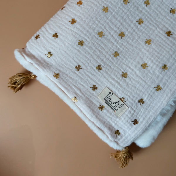 La couverture est une des pièces indispensable du trousseau de bébé. Parfaite en cadeau de naissance ou à s’offrir soit même, cette couverture chaude spéciale “bébés d’hiver”, vous accompagnera très longtemps dans vos moments câlins avec bébé. Les bébés d’hiver qui naissent pendant les mois les plus froids ont besoin d'être tenus bien au chaud à la sortie du ventre de maman. C'est pourquoi nous avons conçu cette couverture chaude spéciale “bébé d’hiver”. Dès son arrivée, bébé passe d'un environnement clos de 37°C à une température extérieure souvent très basse en hiver. C'est pour cela que nos couvertures d'hiver épaisses sont idéales pour réguler et maintenir une bonne température pour le corps de bébé. Comme toutes nos couvertures elle est très souple et enveloppera parfaitement bébé. Cette grande couverture pourra également être utilisée en descente de lit quand bébé sera plus grand. Cette couverture est idéale pour bien réchauffer les bébés d’hiver grâce à sa fausse fourrure extra douce grège, très épaisse (365g/m2), et sa doublure en gaze de coton hypoallergénique au joli petit motif trèfles dorés, un motif plein de sens parfois pour certaines histoires ...  Quatre pompons en laine  dorée viennent sublimer la couverture dans les angles. Ils sont fabriqués à la main pour une pièce encore plus unique. Chaque pompon est posé très fermement avec des points solides afin de garantir une sécurité optimale pour votre enfant.